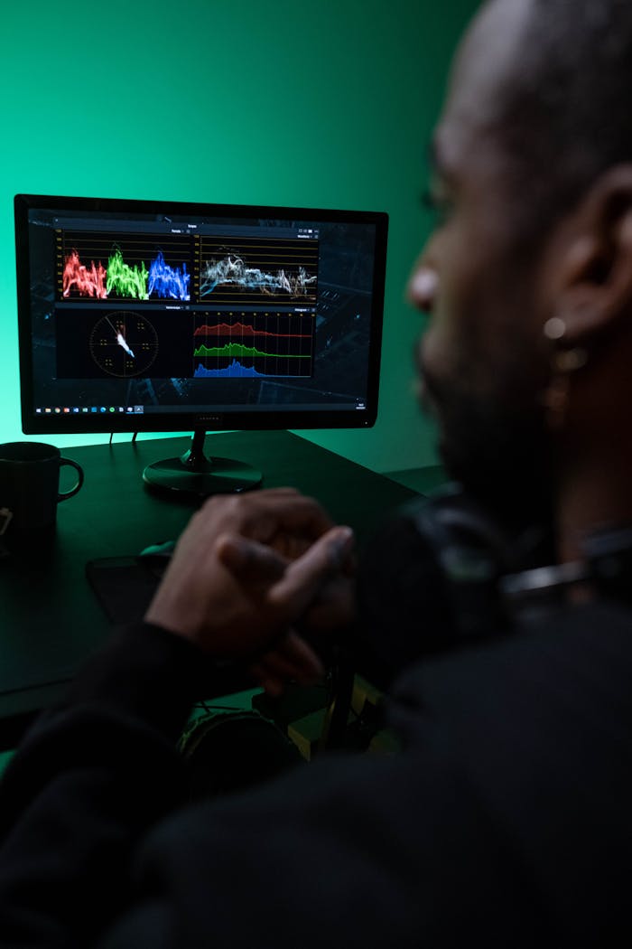 A man intensely studies color-grading graphs on a computer screen in a dimly lit room, highlighting tech analysis.